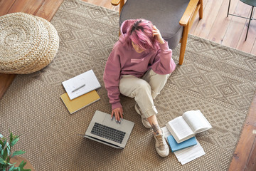 Young hipster teen girl school college student pink hair using laptop computer sit in cozy living room on floor working learning online in internet at home office. Elearning concept. Top view above.