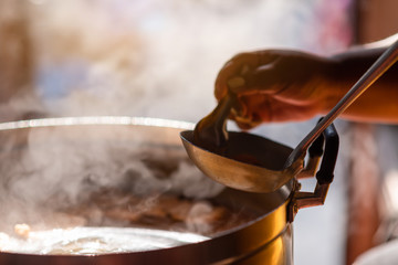 Wall Mural - The chef in the restaurant is cooking while using the dipper in a large pot. The water is boiling and the mass of steam reflected in the morning light.