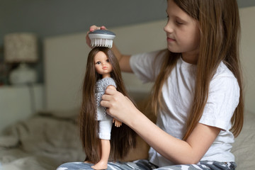 Caucasian girl combing a doll with long hair, a girl playing dolls. Traditional children's games for girls and childhood without gadgets.