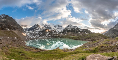 Wall Mural - glacier lake in switzerland in the alps during in the evening sky with clouds and warm lights and a lonely tree