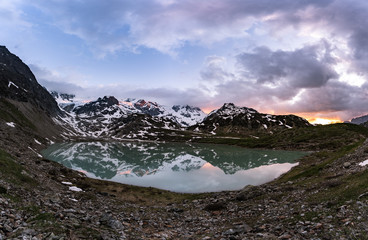 Wall Mural - glacier lake in switzerland in the alps during in the evening sky with clouds and warm lights and a lonely tree