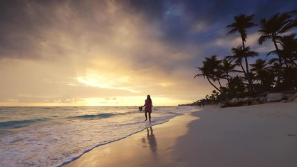 Wall Mural - Tropical vacation on paradise island beach. Happy woman in dress enjoying sea sunrise