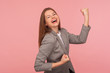 Yes I did it! Portrait of successful enthusiastic young woman in business suit screaming for joy with raised fists, celebrating victory and laughing. indoor studio shot isolated on pink background