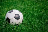 Fototapeta Sport - Soccer ball on the lawn on sunny summer day, close-up. White and black ball on background of green grass, copy space. Concept of active recreation, sports entertainment in nature.