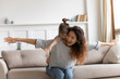 © fizkes - Laughing mother piggybacking little daughter, playing funny game, sitting on cozy couch at home, cute preschool girl hugging from back smiling young mum with hands outstretched pretending plane
