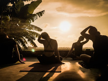 Silhouette Of A Group Of People Doing Yoga At Sunset In The Tropics With Palm Tree And Rice Fields In The Background