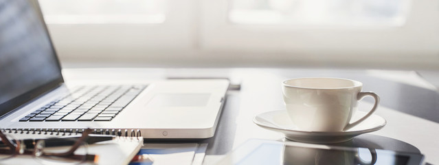 Workplace, laptop computer, coffee cup and digital notebook at office desk, panoramic banner. Business, technology, place of work concept