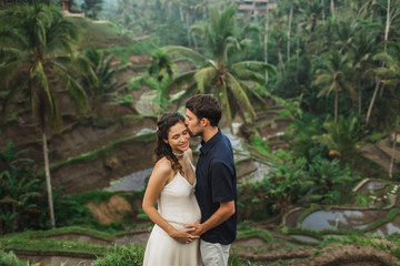 Young latin pregnant woman with husband with amazing view of Ubud rice terraces. Pregnant couple happy together.