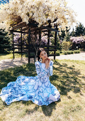 Wall Mural - sensual woman with dark hair in luxurious dress with accessories posing in summer garden with blooming trees