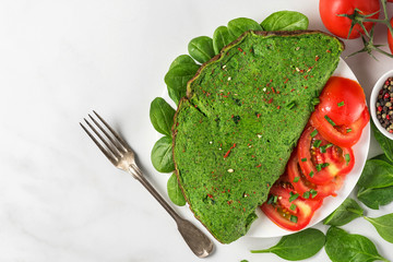 Wall Mural - Healthy green spinach omelette with fresh tomatoes, spices, herbs and fork on white background. ketogenic diet