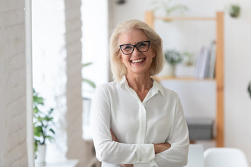 Portrait of smiling senior businesswoman in glasses standing posing in modern office, happy confident middle-aged female employee or CEO look at camera show confidence and success at workplace