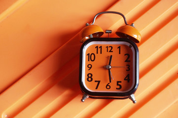 Orange alarm clock on orange plactic background  