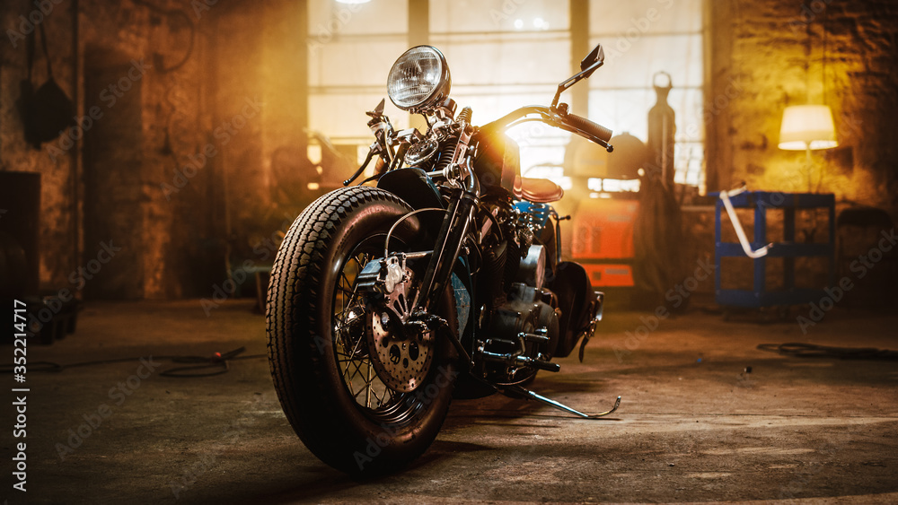Custom Bobber Motorbike Standing in an Authentic Creative Workshop. Vintage Style Motorcycle Under Warm Lamp Light in a Garage. - obrazy, fototapety, plakaty 
