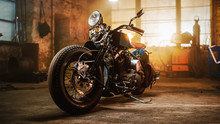 Custom Bobber Motorbike Standing In An Authentic Creative Workshop. Vintage Style Motorcycle Under Warm Lamp Light In A Garage.