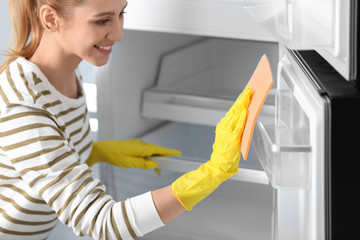 Poster - Woman in rubber gloves cleaning empty refrigerator with rag at home