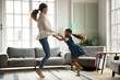 Overjoyed young mom or nanny have fun jumping in living room with excited small girl child, happy playful Caucasian mother dancing relaxing with smiling little daughter, enjoy family weekend at home