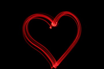 Wall Mural - Long exposure photograph of neon red colour in an abstract heart shape outline, parallel lines pattern against a black background. Light painting photography.