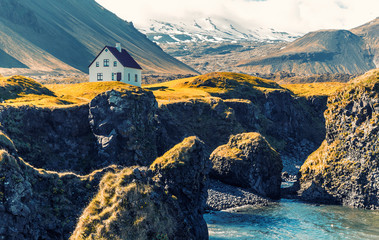 Leinwandbilder - Amazing nature of Iceland. View of the basalt rocks formation on the coastline with beautiful houses and the Mountain Stapafell in the background at Arnarstapi Village in summer sunny day in Iceland