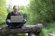 © Tatjana - a man with a laptop sits on a log near the lake