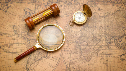 old compass , magnifying glass and sand clock on vintage map
