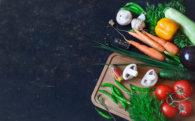 Wall Mural - Healthy food concept with fresh vegetables on a dark background: tomato, zucchini, onion, lettuce, dill, pepper, cucumber, garlic, carrots. Top view with copy space