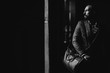 © Dima - A man with a beard in a suit and with a travel bag is in a dark room. Black-and-white photografy