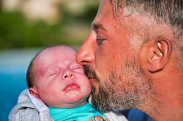 Young father kissing his newborn son outdoor at sunset