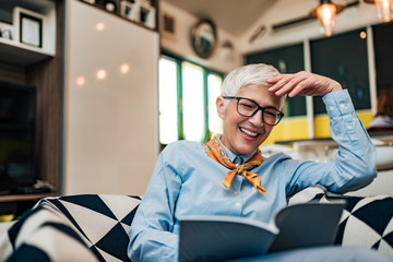 Poster - Close-up portrait of a mature woman laughing while reading a book.