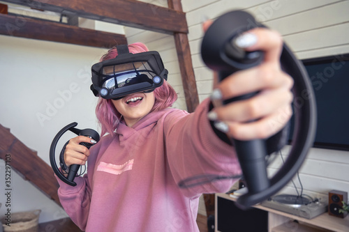 Excited teen hipster girl playing virtual reality video game wear vr goggles headset hold controllers enjoy video game simulator immersive futuristic 3D vr 360 video interactive experience at home.