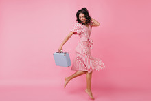 Slender Girl In Great Mood Is Having Fun And Dancing With Bag In Her Hands. Shot Of Italian Model In Wrap Dress On Pink Background