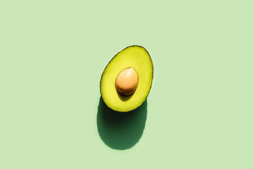 Photo on the topic of natural diet food. Avocado cut in half in sunlight. Neo mint green background. Front view.