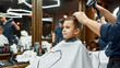 © Svitlana - Kids hairstyle. Little cute boy sitting in armchair at barbershop while barber drying his hair. Getting haircut