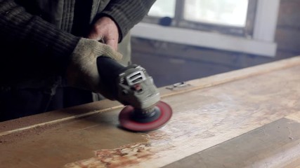 Wall Mural - male artisan polishes a wooden board using a grinding machine in a workshop.