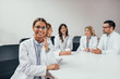 © bnenin - Beautiful smiling female doctor looking at camera while her colleagues are sitting in the background.