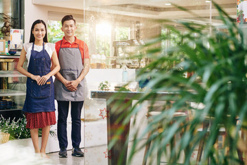 Poster - Happy smiling young Asian couple in aprons working in their cafe