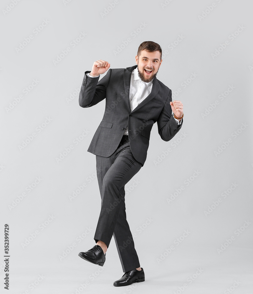 Handsome young businessman dancing against light background