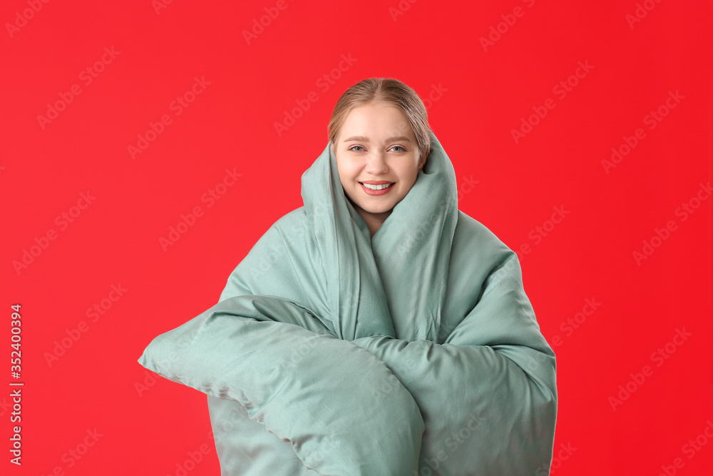 Young woman wrapped in blanket on color background