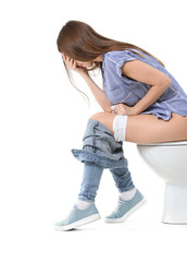 Wall Mural - Young woman sitting on toilet bowl against white background. Concept of hemorrhoids