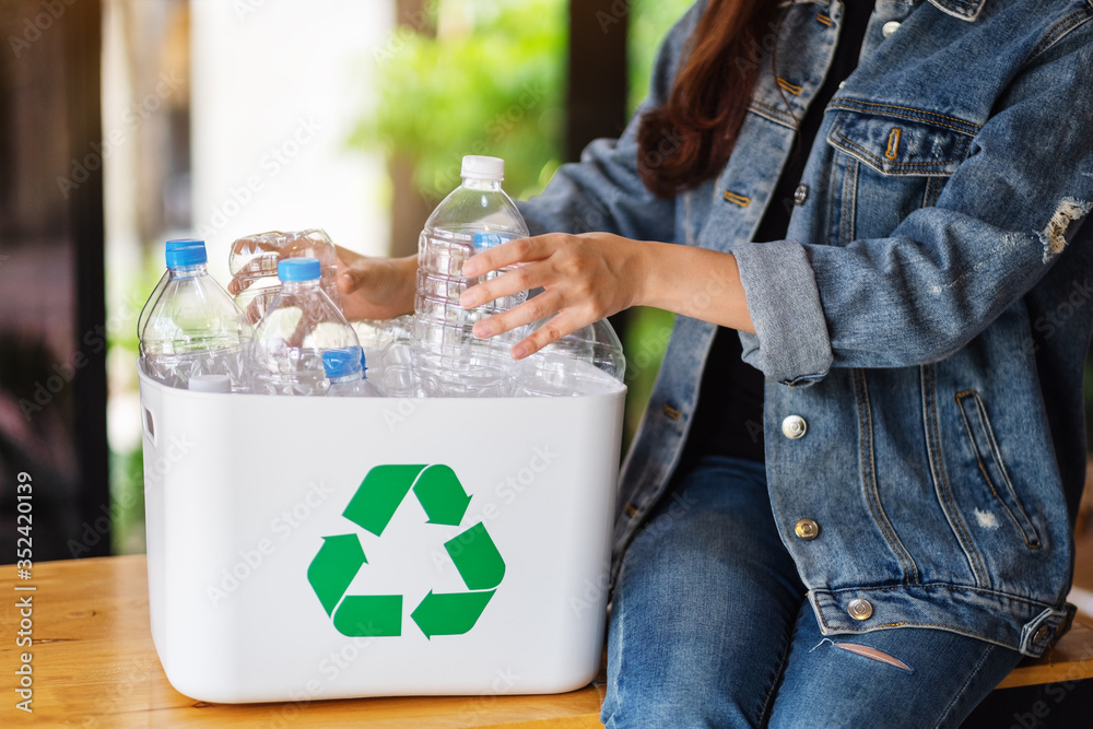 A woman collecting and separating recyclable garbage plastic bottles into a trash bin at home - obrazy, fototapety, plakaty 