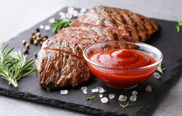 Wall Mural - Beef steak, ketchup and rosemary on a slate board background. Roast beef medium rare.