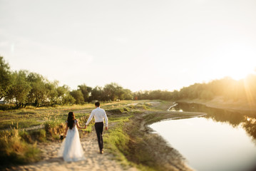 Wall Mural - Wedding photo, wife and husband walking outdoor at sunset 