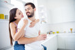 © deagreez - Photo of two people man woman hug embrace piggyback have rest relax weekend man hold mug beverage coffee latte girl sit window sill in kitchen house indoors