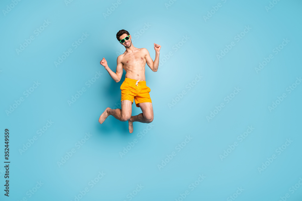 Full length body size view of his he nice attractive cheerful cheery guy in swimming shorts jumping having fun isolated on bright vivid shine vibrant green blue turquoise color background - obrazy, fototapety, plakaty 