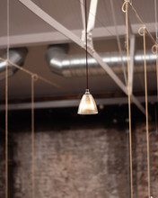A Hanging Lighting Fixture In A Restaurant. An Industrial Style With Exposed Ventilation Pipes And A Red Brick Wall.  