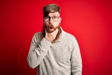 Wall Mural - Handsome Irish redhead man with beard wearing casual sweater and glasses over red background Looking fascinated with disbelief, surprise and amazed expression with hands on chin