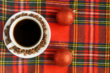 Top view, a cup of black coffee with coffee beans and two red Christmas balls on red heckered background.Chrismas coffee card.Copyspace.