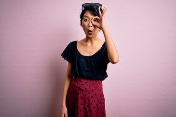 Wall Mural - Young beautiful asian girl wearing casual dress standing over isolated pink background doing ok gesture shocked with surprised face, eye looking through fingers. Unbelieving expression.