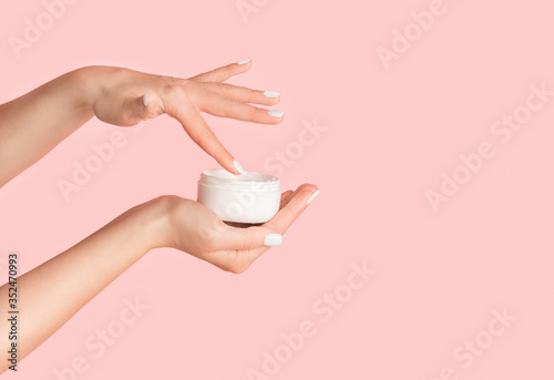 Fotomural Unrecognizable girl applying cream from jar onto her hands against pink backgrou