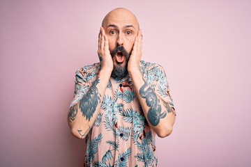 Canvas Print - Handsome bald man with beard and tattoo wearing casual floral shirt over pink background afraid and shocked, surprise and amazed expression with hands on face