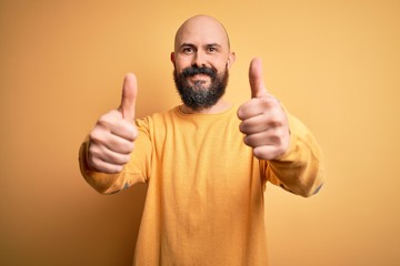 Sticker - Handsome bald man with beard wearing casual sweater standing over yellow background approving doing positive gesture with hand, thumbs up smiling and happy for success. Winner gesture.